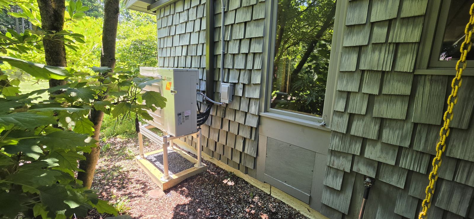 Mitsubishi Hyper-Heat outdoor unit on an aluminum stand beside a shingled home — Superior CO-OP HVAC install