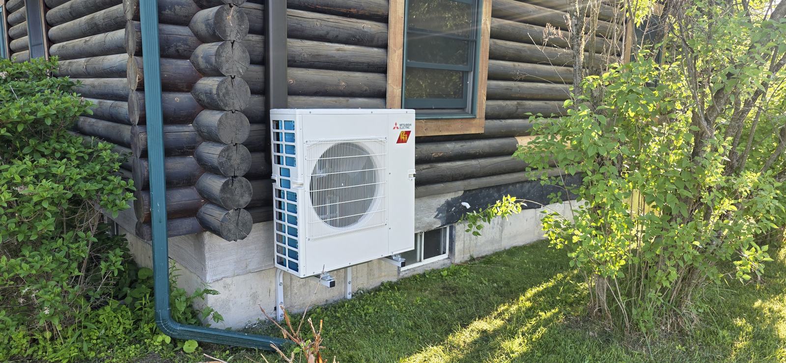 Mitsubishi outdoor unit wall-mounted on a log home — Superior CO-OP HVAC install