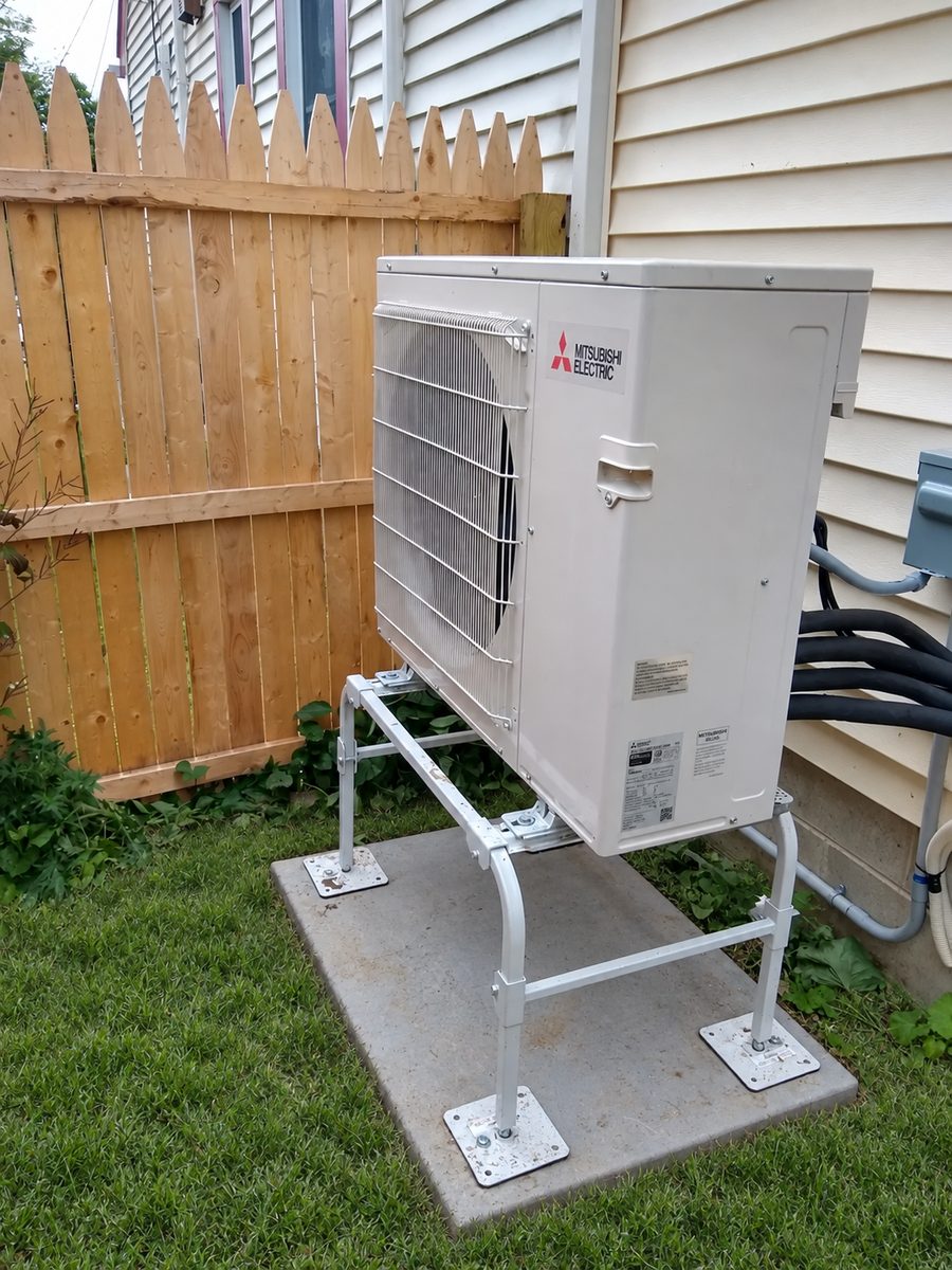 Mitsubishi outdoor heat pump unit mounted on an elevated stand beside a home